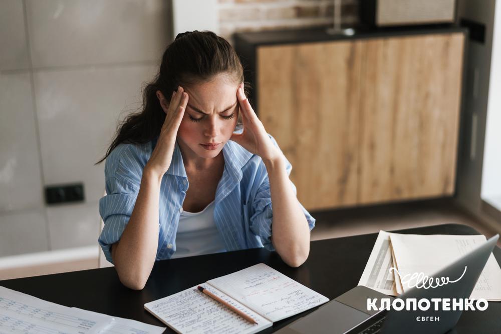 Жінка сидить на робочому місці і тримається за голову